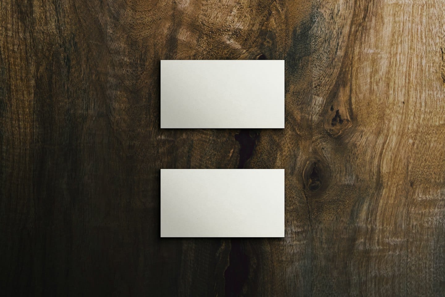 Dos tarjetas de visita en blanco apiladas sobre una mesa de madera.